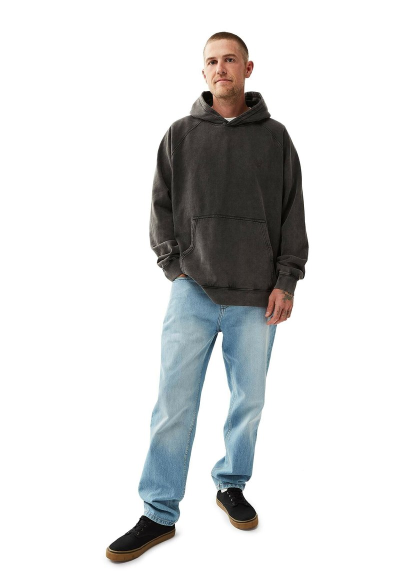 Tummanharmaa huppari, jossa on etutasku, päällä vaaleansiniset farkut ja mustat lenkkarit. Kangas vaikuttaa pehmeältä ja istuu rennosti.