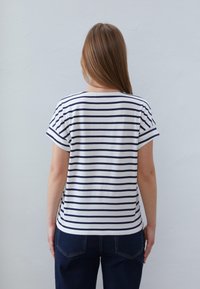 White t-shirt with navy horizontal stripes, soft cotton material, short sleeves, and a relaxed fit, paired with dark blue jeans.