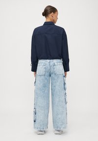 Navy blue collared shirt with long sleeves and adjustable ties; paired with light blue wide-leg cargo jeans featuring side pockets.