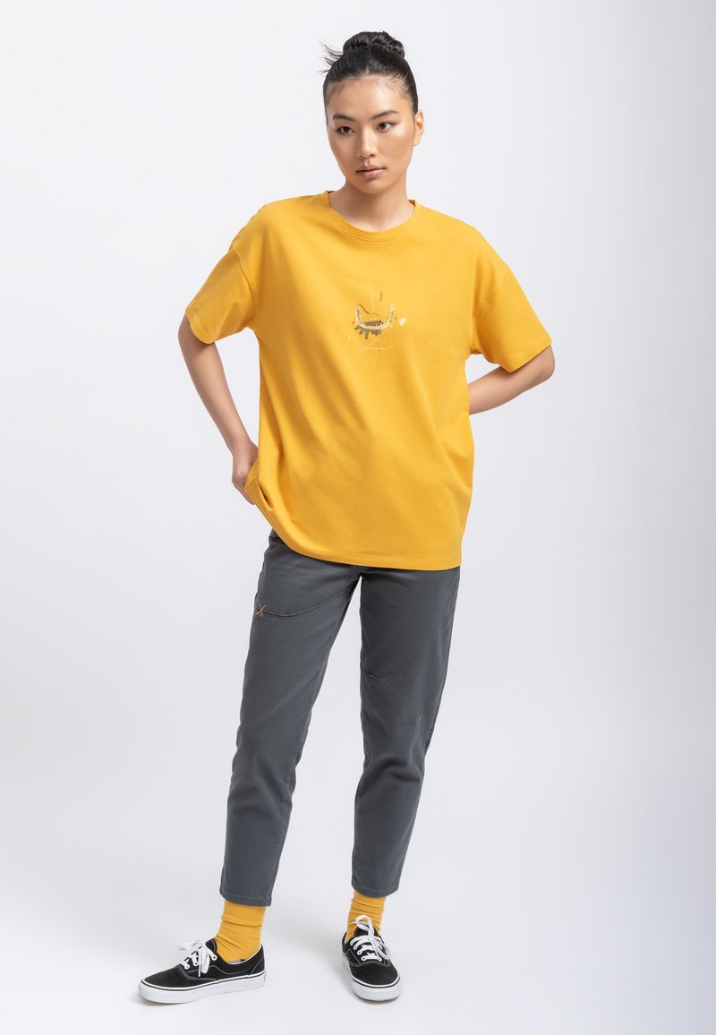 Gele casual t-shirt met korte mouwen met abstract ontwerp. Gecombineerd met grijze, tapered broek en zwarte sneakers.