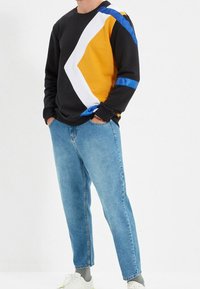 Musta collegepaita, jossa keltaisia, valkoisia ja sinisiä geometrisia kuvioita, yhdistetty vaaleansinisiin farkkuihin ja valkoisiin lenkkareihin. Rentoa istuvuutta.