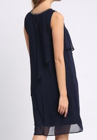 Granatowa sukienka bez rękawów z warstwowym wykończeniem, z otworem w kształcie klucza z tyłu i ozdobnym dekoltem. Wykonana z lekkiej, zwiewnej tkaniny.