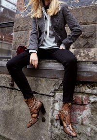 Botines marrones con estampado de serpiente y tacón cuadrado, combinados con pantalones negros y una sudadera gris bajo un blazer de cuadros.