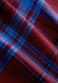 Tissu plié présentant un gros plan d'un motif à carreaux tartan bleu et rouge avec des détails de tissage texturé en diagonale.