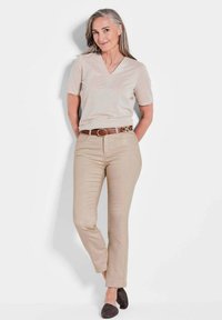 Top beige a maniche corte con scollo a V, pantaloni fitted beige, cintura marrone con dettaglio fibbia e scarpe slip-on scure in tessuto intrecciato. Colori neutri e texture liscia.