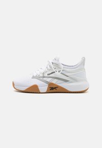 Bílé sportovní boty Reebok s gumovou podrážkou a síťovaným svrškem, šňůrkami a značkovou bočním panelem na čistě bílém pozadí.