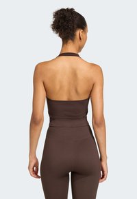 Hnědý halter crop top s přiléhavým střihem, bezšvovou strukturou a krátkou délkou, ve spojení s vysokým pasem a odpovídajícími legínami.