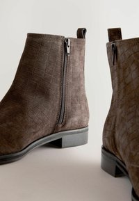 Braune Wildleder-Ankle Boots mit Krokodil-Prägung, seitlichen Reißverschlüssen und einem niedrigen Blockabsatz. Mit Zugschlaufen für einfaches Anziehen.
