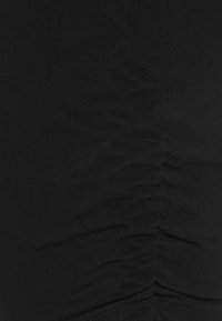 Mustaa kangasta, jossa on rypistynyt tekstuuri, sileä pinta ja näkyvät saumat. Keskity syvään, rikkaaseen väriin ja laskostettuun yksityiskohtaan.