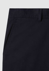 Tissu bleu marine foncé au toucher lisse, avec une taille élastique, des passants de ceinture et des poches latérales. Des coutures sont visibles le long des bords.