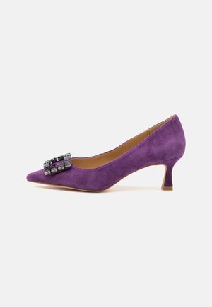 Zapato de ante púrpura con punta afilada, que presenta un broche decorativo negro y púrpura en la parte frontal y un tacón de aguja de altura media.