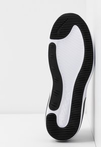 Sole of a black and white Nike Air Max sneaker with textured grip pattern leaning against a white corner wall.