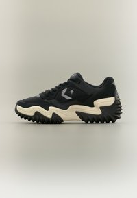 Μαύρο αθλητικό παπούτσι με υφή στο σχέδιο, διαθέτοντας χοντρή κρέμα σόλα και έντονο λογότυπο αστεριού. Στρογγυλεμένη μύτη και επενδυμένος γιακάς για άνεση.