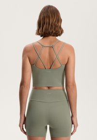 Zöld sportos crop top állítható, keresztbe futó pántokkal és hozzáillő, magas derekú sorttal, sima, rugalmas anyagból készült.