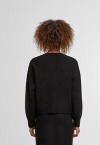 Črni pleteni pulover z raztegljivo prileganjem, z rebrastim robom in manšetami. Mehak tekstura, okrogli izrez in minimalističen dizajn.