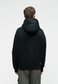 Sweatshirt preto com um capuz grande, feito de tecido macio. Apresenta um pequeno logótipo branco da Nike no canto inferior direito, com um corte descontraído.
