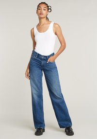 Laialt jalaga sinised denim teksad kõrge vöökohaga, esikummutid ja klassikaline lõige, koos valge sobiva sifonktopiga.