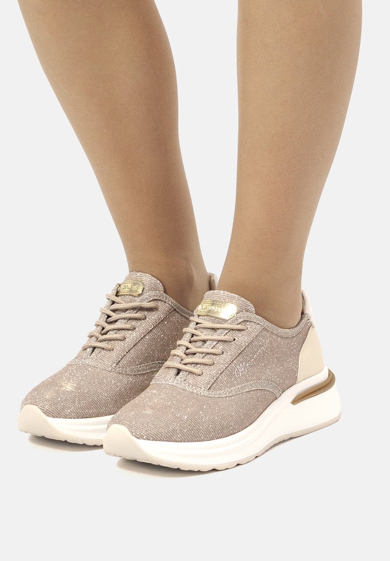 Baskets de sport beige clair avec un dessus en textile pailleté, bout rond et semelles blanches. Elles possèdent des lacets et un subtil accent métallique sur le talon.