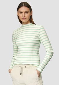 Haut à rayures à manches longues en tissu ribbed vert clair et crème, avec un col montant et une silhouette ajustée, porté avec un pantalon crème décontracté.