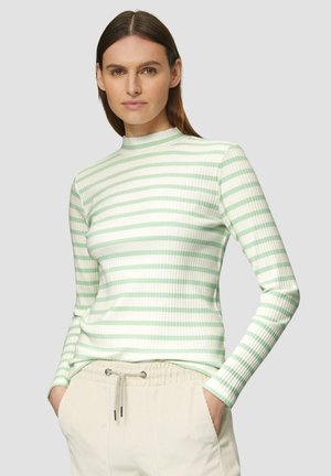 Haut à rayures à manches longues en tissu ribbed vert clair et crème, avec un col montant et une silhouette ajustée, porté avec un pantalon crème décontracté.