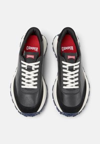 Sneakers in pelle nera con lacci bianchi e marchio "Camper" rosso sulle solette. Suole tonde e testurizzate in colori a contrasto.