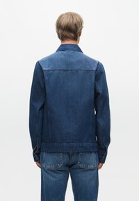 Τζάκετ από τζιν με σκούρο μπλε πλύσιμο, κουμπιά μπροστά και κλασικό γιακά. Διαθέτει ραφές στους ώμους και εφαρμοστή γραμμή. Φοριέται με ταιριαστά τζιν.