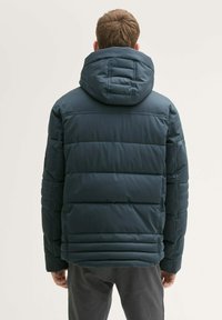 Mornarska puhovka s kapuco, ki ima kvadratne panele in nekoliko sijajno površino. Namenjena je toplini, z udobnim krojem in dolgimi rokavi.