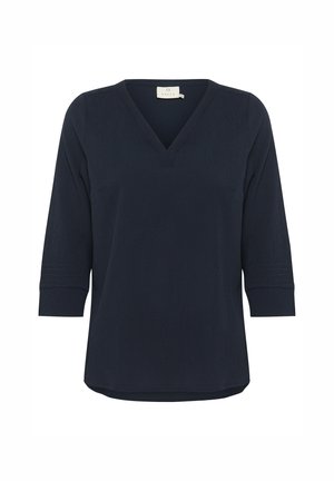 Tamsiai mėlyna V-žalias viršus pagamintas iš minkštos medžiagos, turintis trijų ketvirčių rankoves su tekstūriniu detalizavimu ant rankogalių ir apvaliu kraštu.