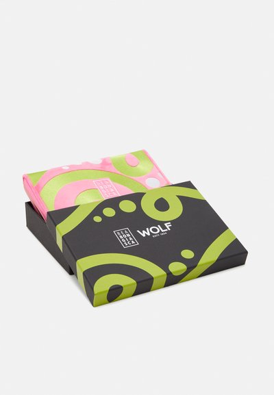Packaging with a black box featuring green swirls and text. Inside, a pink item with large green and white circles is visible.