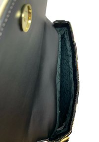 Svart läderhandväska med en mörkgrön mönstrad foder och guldfärgade detaljer. Har en rymlig fack och en strukturerad design.