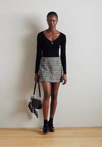 Top aderente nero a maniche lunghe, gonna corta in tweed testurizzato nei colori nero, bianco e blu. Indossa calze nere e scarpe, mentre tiene una borsa piccola.