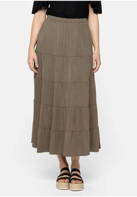 Falda maxi marrón en capas con cintura elástica, que presenta una tela suave y sutiles detalles de costura horizontal. Combinada con sandalias de plataforma negras.