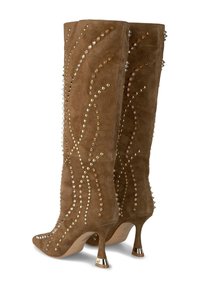 Botas altas de gamuza marrón que llegan hasta la rodilla, con punta afilada, adornadas con tachuelas doradas y plateadas en un patrón ondulado, y un acento de tacón metálico.