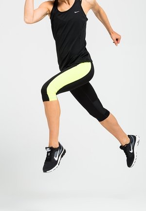 Zwarte sportieve tanktop met een Nike-logo, gecombineerd met zwarte en neongele capri-legging, en zwarte hardloopschoenen met witte accenten.