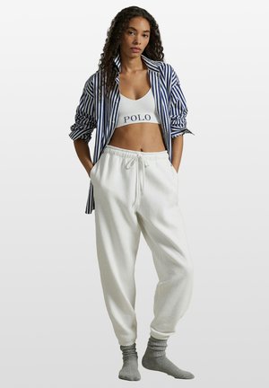 Hvide joggingbukser med elastisk taljebånd, kombineret med en hvid croppet top med "POLO"-logo og en blå- og hvide stribet skjorte. Grå sokker.
