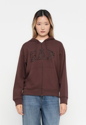 Rudas zip-up džemperis su juodu leopardų raštu „GAP“ logotipu, ilgomis rankovėmis ir reguliuojamu gobtuvu. Minkšta medžiaga, laisvas kirpimas.