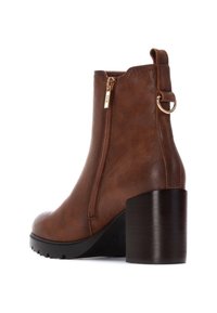 Stivale alla caviglia in pelle marrone con zip laterale, punta tonda e tacco testurizzato nero. Presenta un occhiello per la presa e dettagli in metallo color oro.