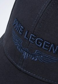 Casquette noire avec broderie "PME LEGEND" et motif ailé. Présente un tissu texturé et une visière incurvée, avec des coutures détaillées.