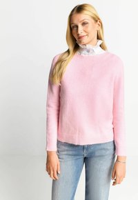 Helles rosa Sweatshirt mit weicher Textur, Rundhalsausschnitt, geripptem Saum und langen Ärmeln, kombiniert mit hellblauen Jeans. Weißer Rüschkragen sichtbar.