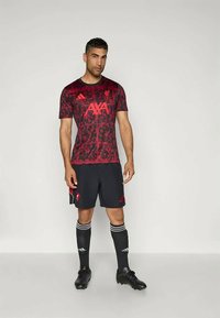 Rød atletisk trøje med blomstermønster, parret med sorte shorts, sorte støvler og sorte knæstrømper med hvide striber.