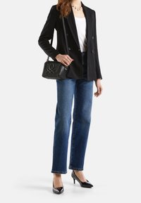 Svart dubbelknäppt kavaj över en vit topp, i kombination med blå raka jeans och svarta lackskor med klack. Liten strukturerad svart handväska.