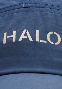 Blauwe stoffen pet met witte hoofdletters "HALO" gedrukt op het voorpaneel, met zichtbare stiksels en textuur.