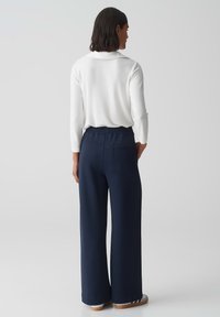 Witte langemouwen top met een subtiele textuur, gecombineerd met marineblauwe wijde broek met een elastische tailleband en een achterzak.