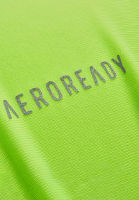 Fluoreszierender grüner Stoff mit strukturierter Oberfläche, auf dem das Wort "AEROREADY" in silberner, metallischer Schrift in der Mitte erscheint.