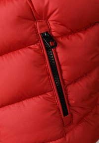 Sarkans pūkains džemperis ar vertikālu melnu rāvējslēdzēju un izšūtu quilted modelēšanu. Audums izskatās gluds un spīdīgs ar izolācijas tekstūru.