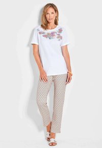 T-shirt en coton blanc avec une broderie florale colorée sur la poitrine, associé à un pantalon beige à motifs avec des motifs en forme de goutte d'eau bleus.