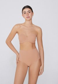 Top bez ramínek v tělové barvě se tvarovanými košíčky a bezšvovým designem, zkombinovaný s vysokým pasem odpovídajícími kalhotkami pro hladký siluetu.
