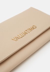 Beige teksturert lommebok med hevet gull "VALENTINO"-logo. Glatt lukke med sydd detalj langs omkretsen.