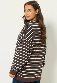 Haut à manches longues rayé marron et crème avec une coupe décontractée, présentant un col rond et des poignets côtelés. Tissu doux avec un design décontracté.