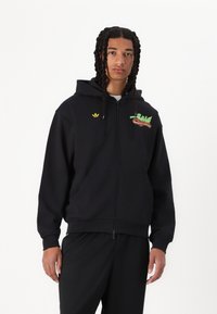 Sweatshirt preta com fecho zip em mistura de algodão, apresentando um bolso frontal, punhos canelados e um logótipo bordado da Adidas no peito.